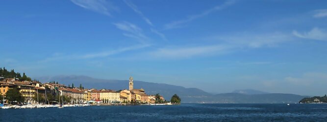 Trip Russland beliebte Urlaubsziele am Gardasee -  Mit einer Fläche von 370 km² ist der Gardasee der größte See Italiens. Es liegt am Fuße der Alpen und erstreckt sich über drei Staaten: Lombardei, Venetien und Trentino. Die maximale Tiefe des Sees beträgt 346 m, er hat eine längliche Form und sein nördliches Ende ist sehr schmal. Dort ist der See von den Bergen der Gruppo di Baldo umgeben. Du trittst aus deinem gemütlichen Hotelzimmer und es begrüßt dich die warme italienische Sonne. Du blickst auf den atemberaubenden Gardasee, der in zahlreichen Blautönen schimmert - von tiefem Dunkelblau bis zu funkelndem Türkis. Majestätische Berge umgeben dich, während die Brise sanft deine Haut streichelt und der Duft von blühenden Zitronenbäumen deine Nase kitzelt. Du schlenderst die malerischen, engen Gassen entlang, vorbei an farbenfrohen, blumengeschmückten Häusern. Vereinzelt unterbricht das fröhliche Lachen der Einheimischen die friedvolle Stille. Du fühlst dich wie in einem Traum, der nicht enden will. Jeder Schritt führt dich zu neuen Entdeckungen und Abenteuern. Du probierst die köstliche italienische Küche mit ihren frischen Zutaten und verführerischen Aromen. Die Sonne geht langsam unter und taucht den Himmel in ein leuchtendes Orange-rot - ein spektakulärer Anblick.